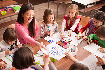 Frau arbeitet mit Kindern am Tisch