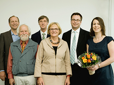 Gruppenbild mit zwei Frauen und vier Männern, eine Frau hält einen Blumenstrauß vor sich.