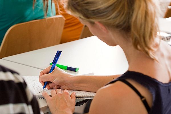Eine Studierende macht sich in einem Seminarraum Notizen.